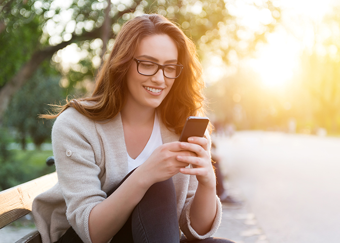 A woman sitting outside and using her phone.