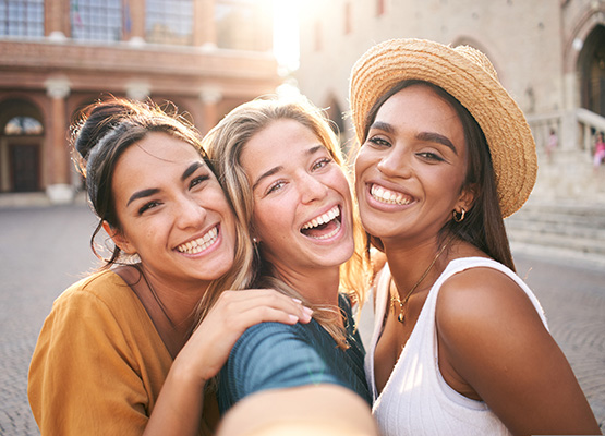 Three women smiling and taking a selfie outside.
